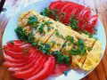 Pyszne koreańskie śniadanie: pokrojony omlet z jajek posypany szczypiorkiem, podany z plasterkami pomidora.