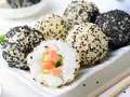 Szybkie sushi w kulkach, obtoczone białym i czarnym sezamem. Jedna kulka jest przekrojona, ukazując łososia i ogórek.