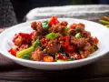 Chrupiący kurczak po kantonsku z papryczkami chili i zieloną cebulką na białym talerzu.