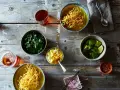 Dwa miseczki khao soi, świeża kolendra, limonki, jajko na twardo, czerwona cebula i płatki chili na drewnianym stole.