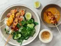 Pyszny kurczak satay na ryżu z orzeszkami ziemnymi, ogórkiem i limonką. Obok miseczka z sosem orzechowym.