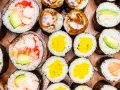 Różnorodne rolki sushi: grubsze futomaki z krewetkami i awokado, cieńsze hosomaki z łososiem, awokado, żółtą rzodkwią i polane sosem.