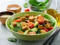Sałatka ze szpinakiem, pomidorkami, ogórkiem i kostkami **butter tofu**, posypana sezamem.