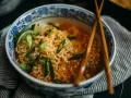 Aksamitny makaron lau thai w misce z niebieskimi zdobieniami, udekorowany szczypiorkiem, chili i limonką.