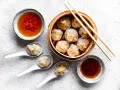 Pyszne dim sum w bambusowym parowniku, podane z sosem chili i sosem sojowym. Trzy pierożki na łyżeczkach zachęcają do spróbowania.
