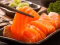 Sashimi co to? Świeże, pomarańczowe kawałki łososia podniesione pałeczkami, obok zielonej pasty wasabi i natki pietruszki.