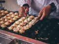 Ręce obracają kulki takoyaki na specjalnej patelni. Ten prosty takoyaki przepis jest w trakcie realizacji.