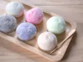 Kolorowe desery azjatyckie, mochi, ułożone na drewnianej tacy.