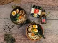 Dwie miski aromatycznego makaronu ramen z sosem sojowym, jajkiem, mięsem i wodorostami. Obok opakowanie makaronu i butelka sosu.