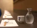 Sake ile procent? Delikatna czarka i karafka z sake czekają na degustację. W tle rząd nakryć.