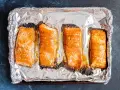 Cztery kawałki pieczonego łososia na folii aluminiowej. Idealny łosoś do sushi, lekko przypieczony na brzegach, zachęca do przygotowania.