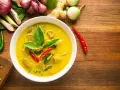 Aksamitne tajskie curry z tofu, ozdobione świeżą bazylią i papryczkami chili, otoczone składnikami jak galangal i trawa cytrynowa.