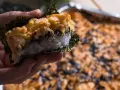 Dłoń trzyma kawałek sushi bake z ryżem, nori i zapiekanym farszem.
