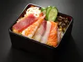 Chirashi zushi: kolorowe plastry ryb (tuńczyk, łosoś, biała ryba), krewetka, plasterki ogórka i lotosu na ryżu.