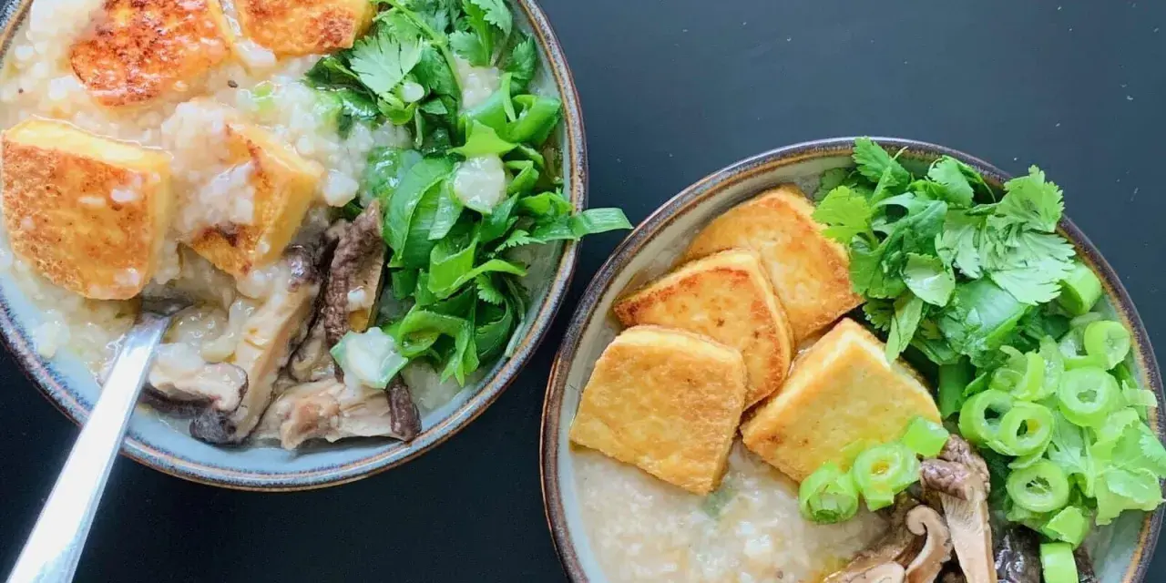 Dwie miseczki aromatycznego congee z chrupiącym tofu, grzybami i świeżymi ziołami.