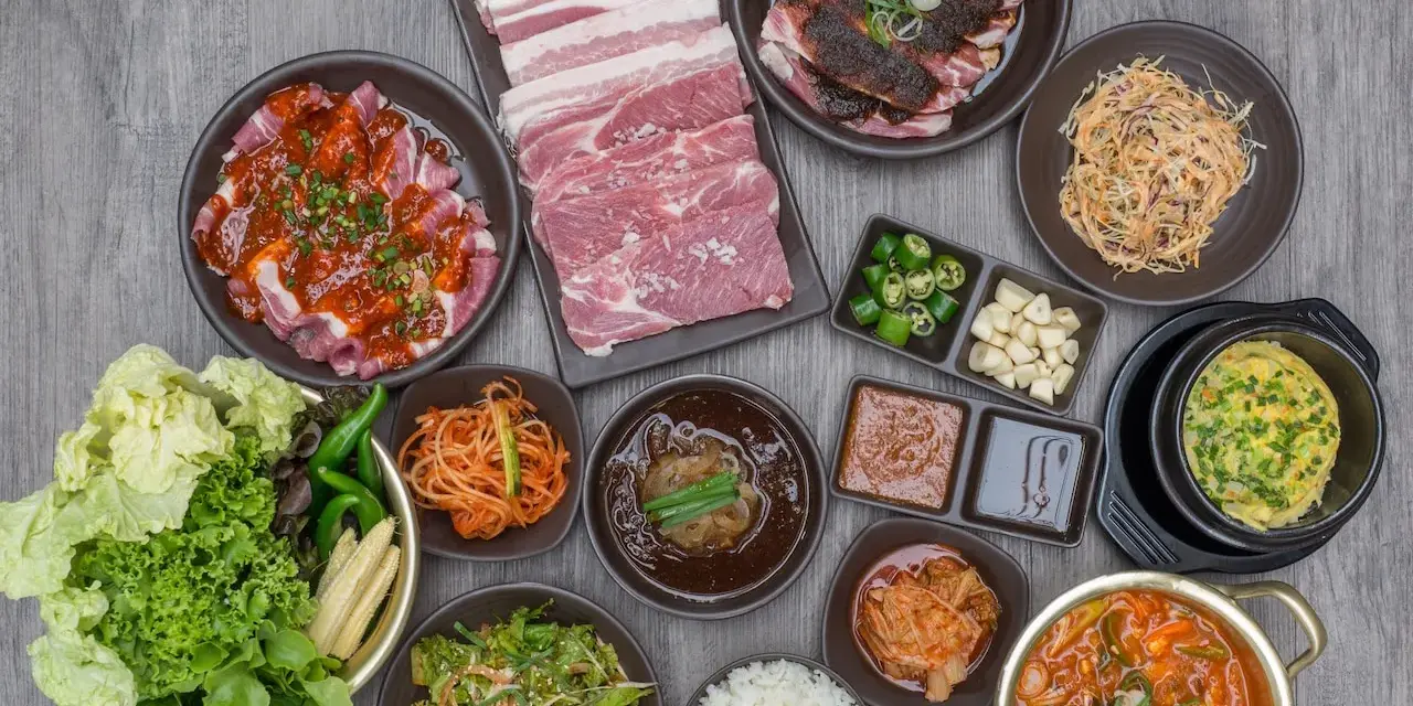 Obfity zestaw do korean bbq: surowe i marynowane mięso, kimchi, sałatki, ryż i dodatki.