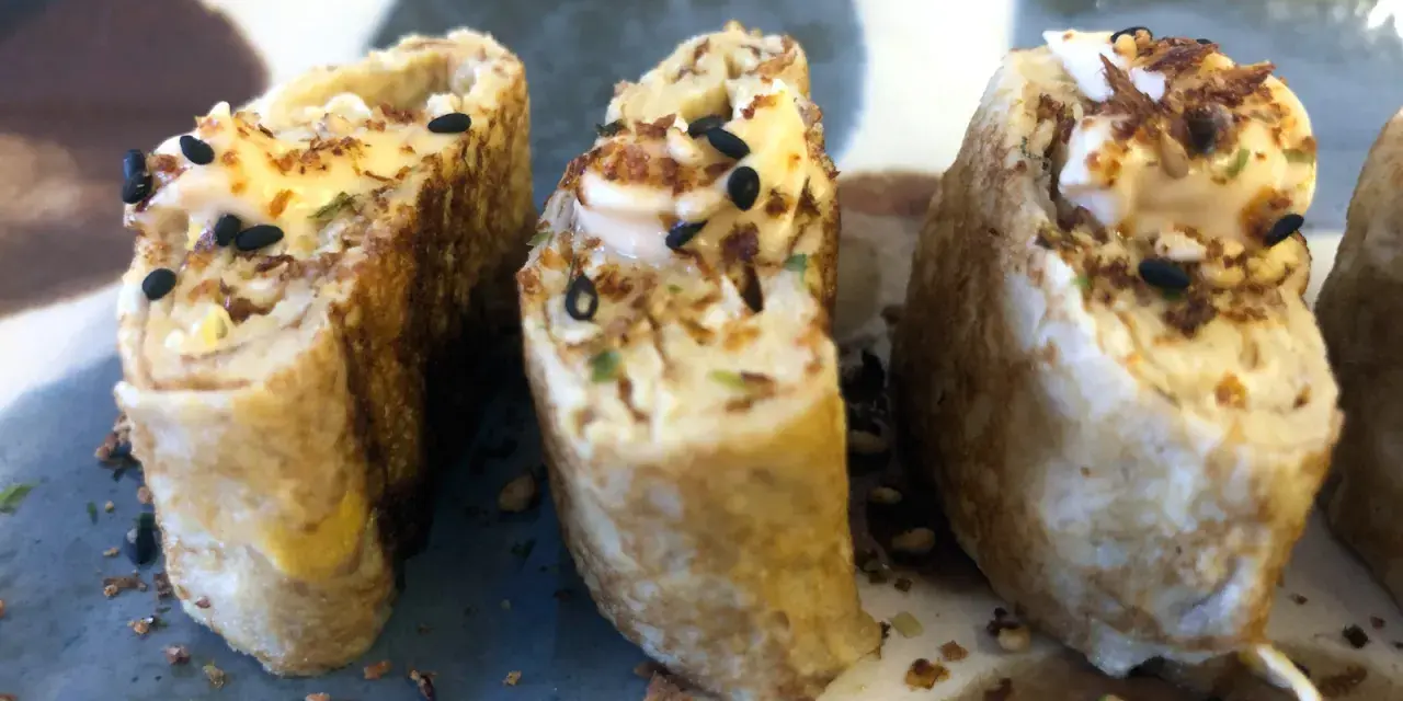 Trzy kawałki sushi w omlecie, polane majonezem i posypane czarnym sezamem.