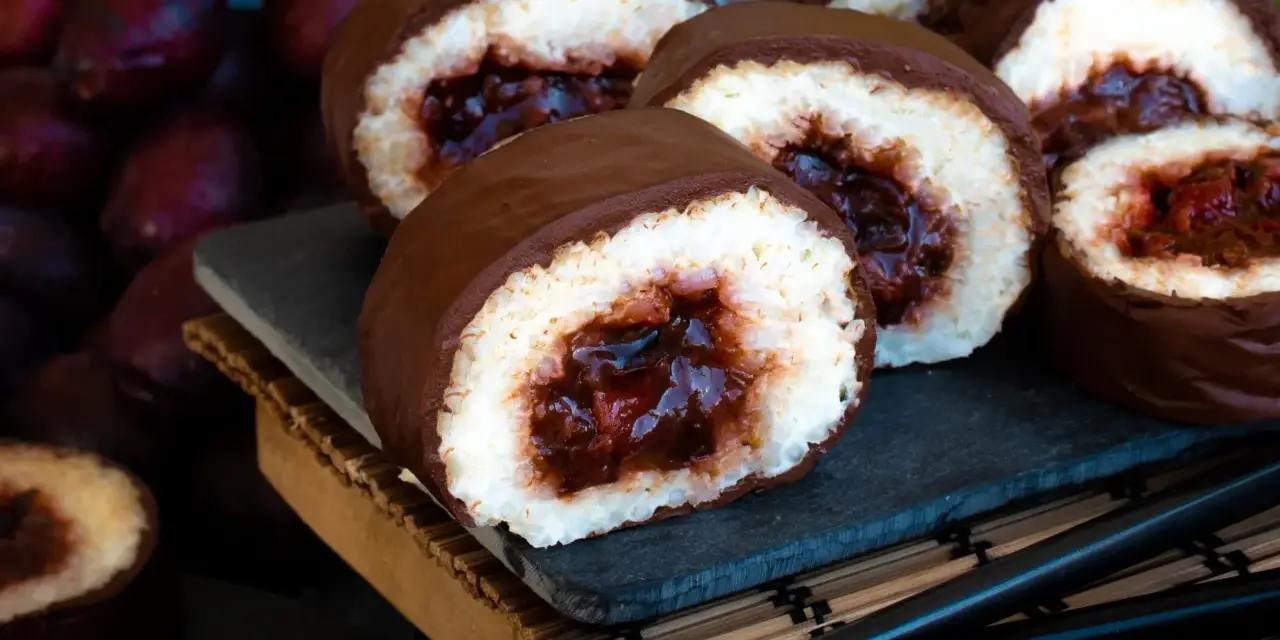 Słodkie rolki sushi na słodko, oblane czekoladą, z owocowym nadzieniem. Obok ciemne owoce i pałeczki.
