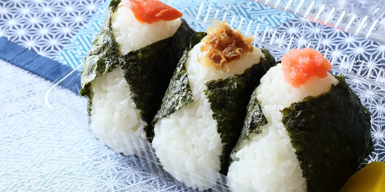 Trzy onigiri z ryżem, zawinięte w nori, z łososiem, tuńczykiem i ikrą na wierzchu. Idealne na przekąskę.