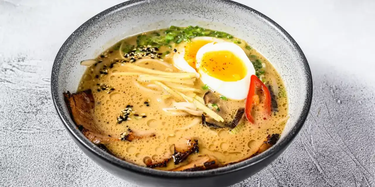 Miseczka aromatycznej zupy ramen z jajkiem na pół, plastrami mięsa, grzybami i szczypiorkiem.