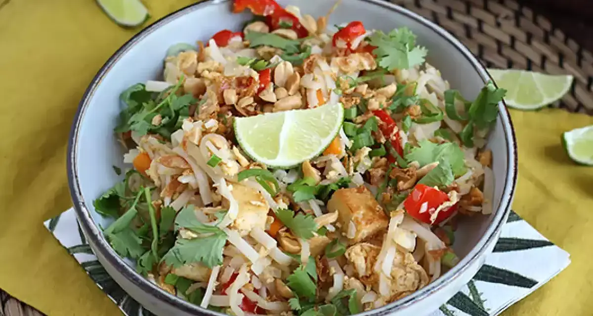 Pyszne pad thai z tofu, posypane orzeszkami ziemnymi i świeżą kolendrą, z kawałkami limonki.
