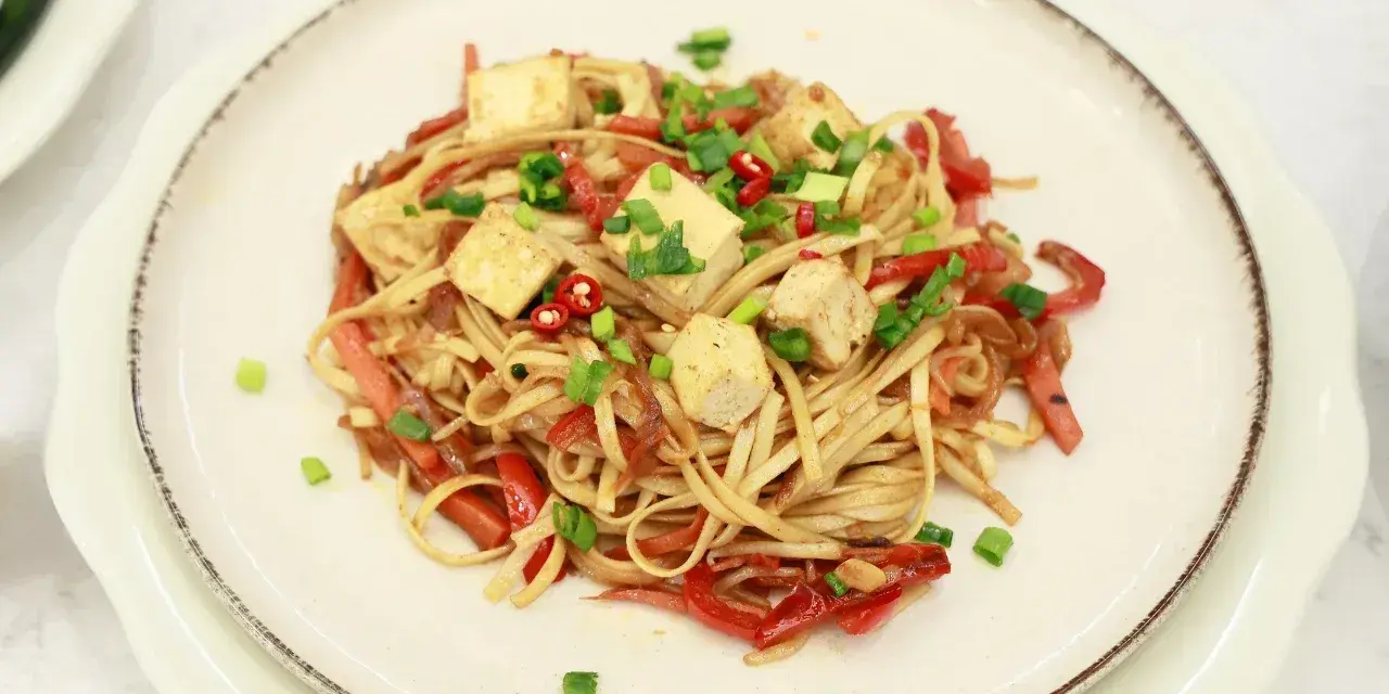 Smażony makaron Chow Mein z tofu, papryką i szczypiorkiem na talerzu.