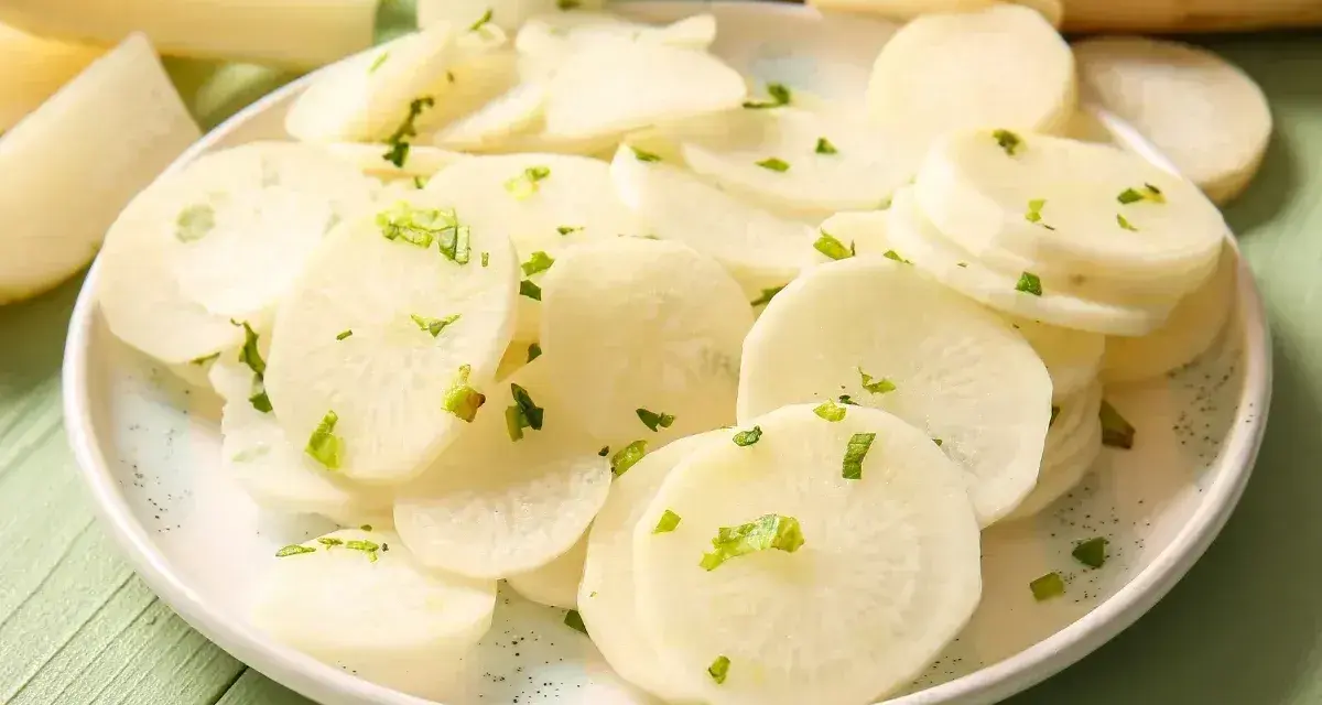 Plasterki białej rzodkwi, czyli daikon, posypane zielonymi ziołami na talerzu.
