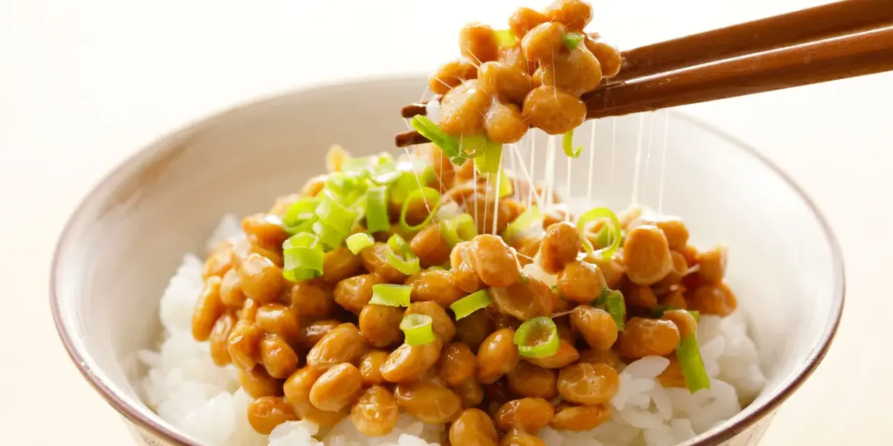 Miseczka ryżu z natto, japońską potrawą z fermentowanej soi, posypana szczypiorkiem. Pałeczki unoszą nitki natto.