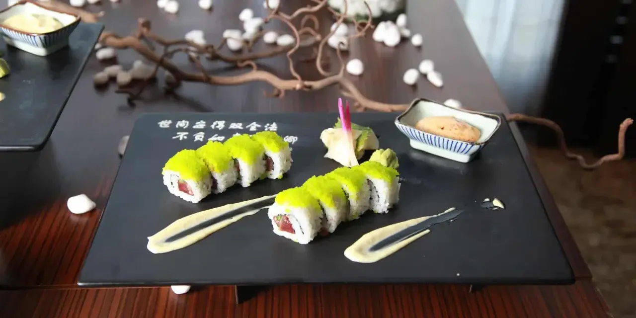 Dwa rzędy sushi z zielonym ikrą, podane z sosem i imbirem. Idealny sposób, jak podawać sushi na eleganckim talerzu.