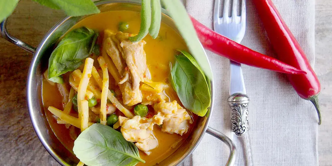Aromatyczne czerwone curry z kurczakiem, bambusem i groszkiem, ozdobione świeżą bazylią i papryczkami chili.