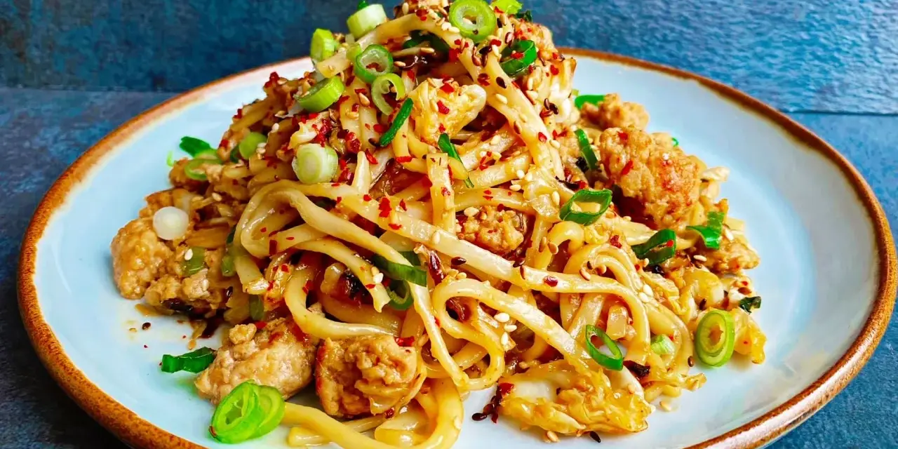 Pyszny makaron z wieprzowiną, posypany szczypiorkiem i sezamem, z dodatkiem płatków chili.