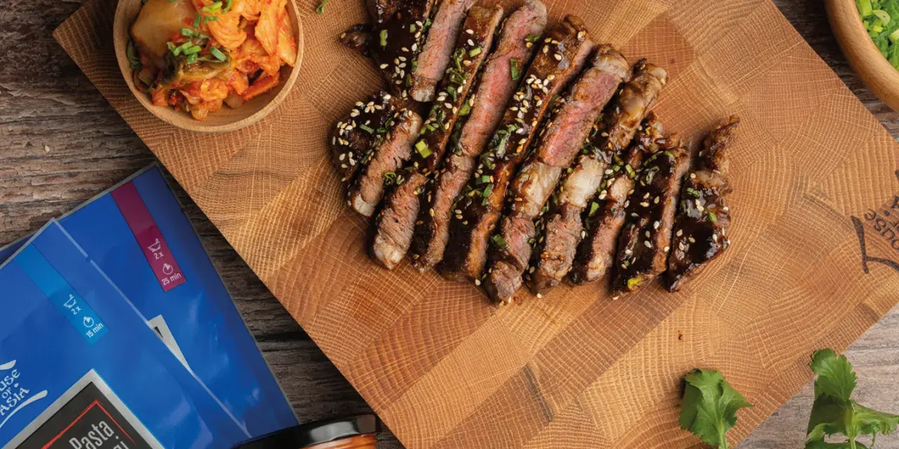 Pokrojony stek bulgogi polany sosem, obok miseczka z kimchi i opakowanie pasty do bulgogi.