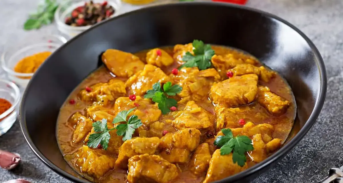 Aksamitny kurczak w sosie curry, jedno z popularnych potraw kuchni azjatyckiej, ozdobiony natką pietruszki i różowym pieprzem.