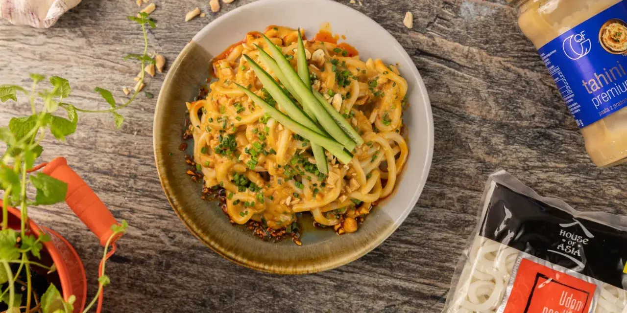 Udon co to? Makaron udon w kremowym sosie z orzeszkami ziemnymi i ogórkiem, obok paczka makaronu i tahini.