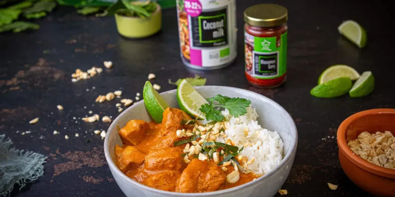 Aksamitny kurczak w sosie massaman curry, podany z ryżem, limonką i posypany orzeszkami. Obok puszka mleka kokosowego i słoiczek pasty massaman.
