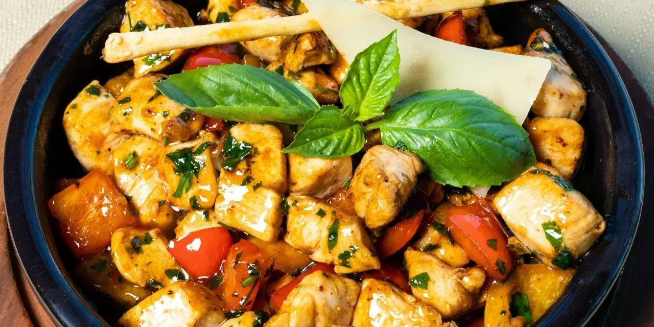 Kawałki kurczaka w sosie z papryką i ziołami, ozdobione listkami bazylii i paluszkami grissini. Danie przypomina egzotyczne jungle curry.