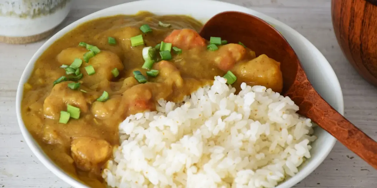 Pyszne japońskie curry z kurczakiem i warzywami, podane z ryżem i posypane szczypiorkiem.