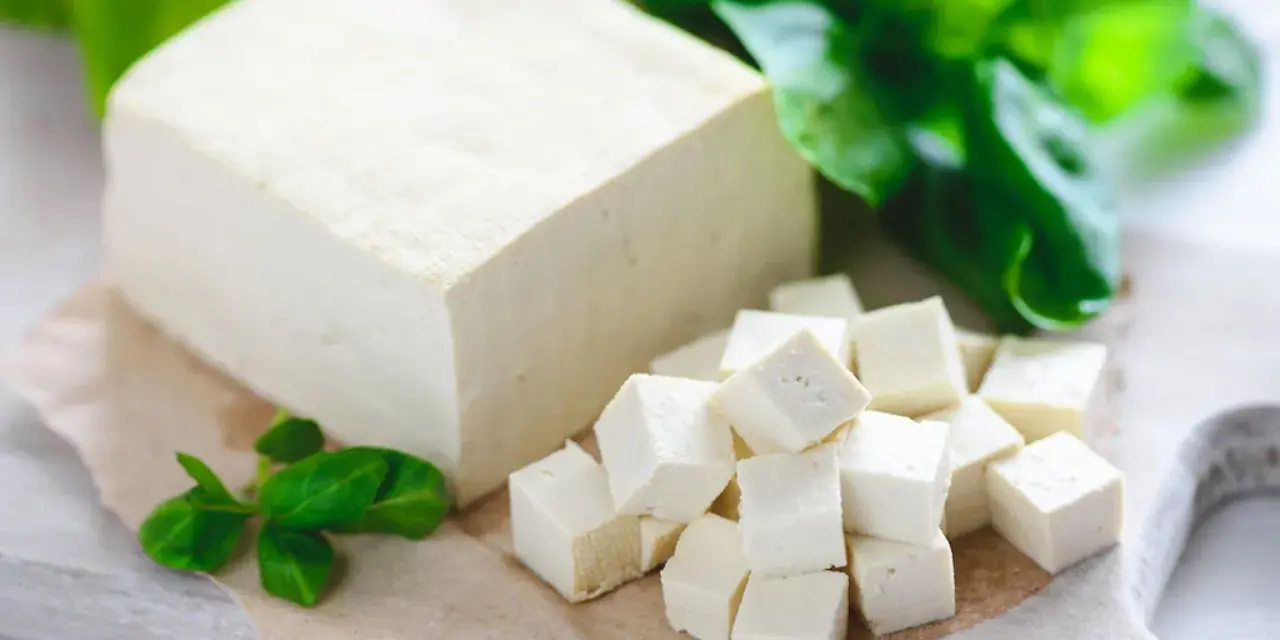 Kostka i pokrojone w kostkę tofu, obok zielone listki. Tak wygląda tofu – białe, delikatne, gotowe do przygotowania.