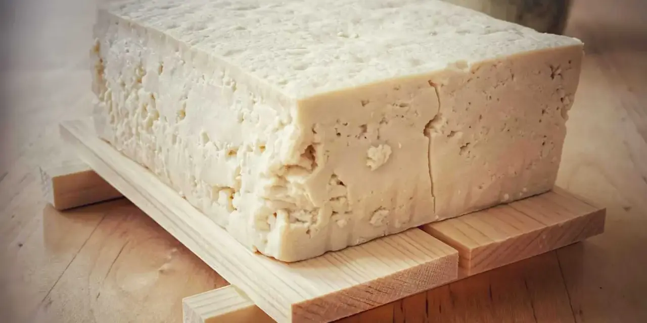 Duży blok domowego tofu na drewnianej podstawce, gotowy do przygotowania pysznych dań.