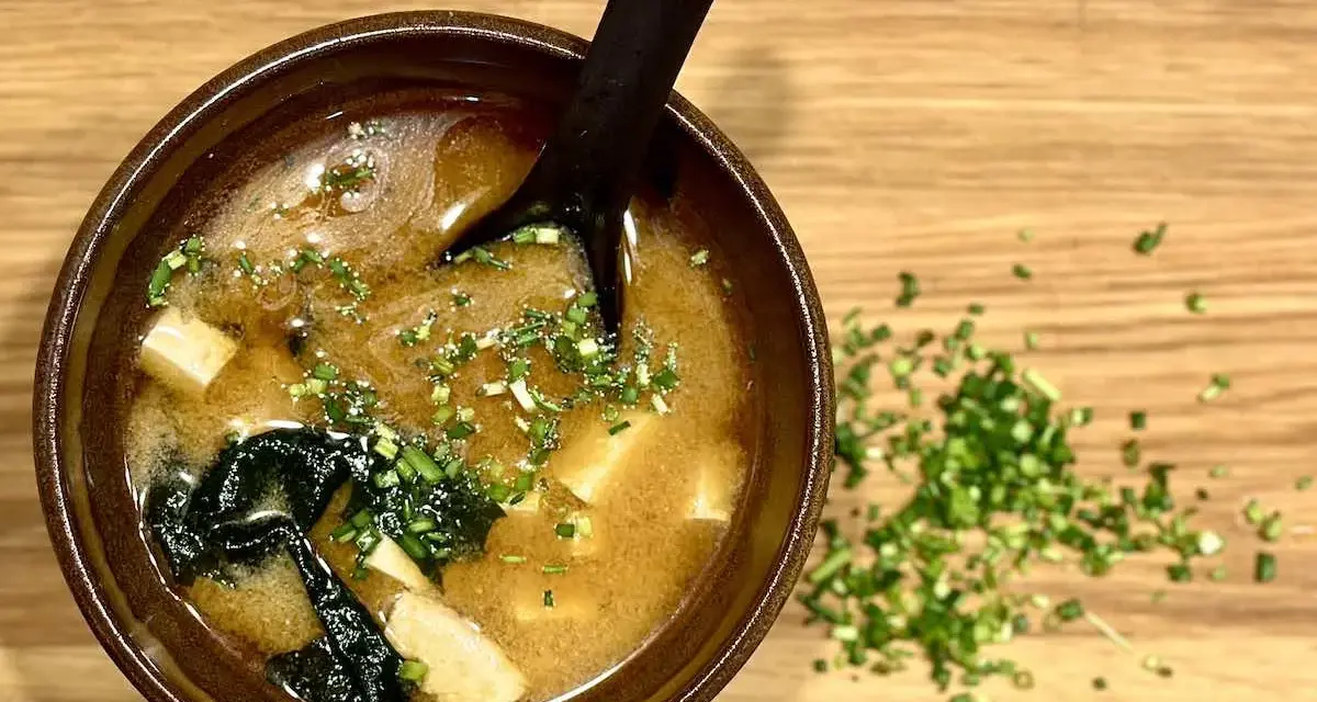 Miseczka aromatycznego miso shiru z tofu i wodorostami, posypana szczypiorkiem.