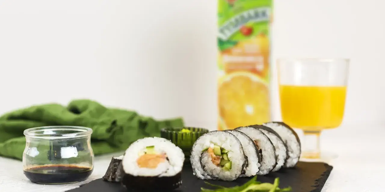Pyszne sushi z łososiem, ogórkiem i ryżem, podane z sosem sojowym i sokiem pomarańczowym.