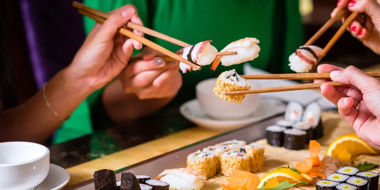 Ręce trzymają pałeczki, jedząc sushi. To smakowita uczta, która odzwierciedla japońskie tradycje kulinarne.