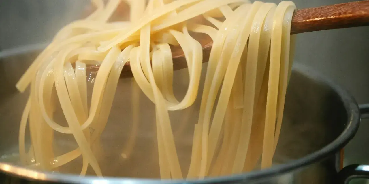 Gorący makaron mie unoszony na drewnianej łyżce nad parującym garnkiem. Idealny przepis na szybki obiad.