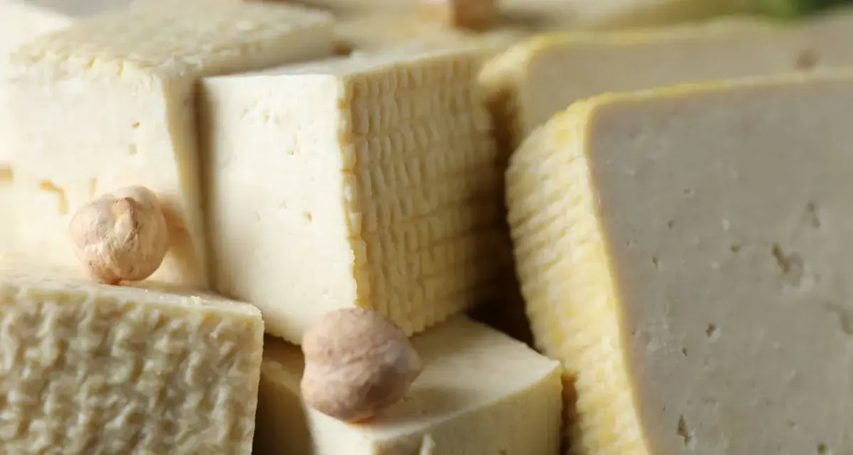 Kawałki miękkiego tofu ułożone obok siebie, niektóre z nich mają kratkowaną fakturę. Kilka ciecierzycy dodaje uroku.