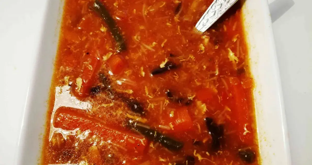 Aksamitna zupa ostro kwaśna z kawałkami warzyw i jajka, podana w białej misce.