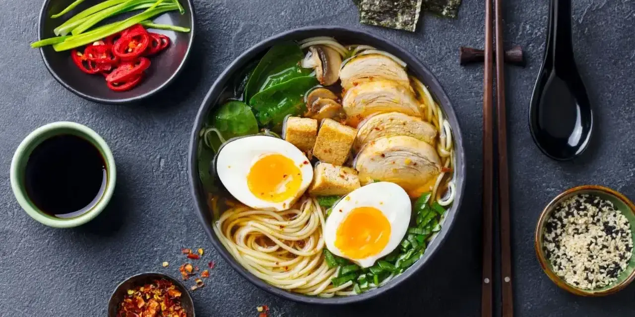 A miseczce aromatycznego ramenu z tofu, jajkiem na pół, kurczakiem i zieloną cebulką. Obok sos sojowy, chili i nori.