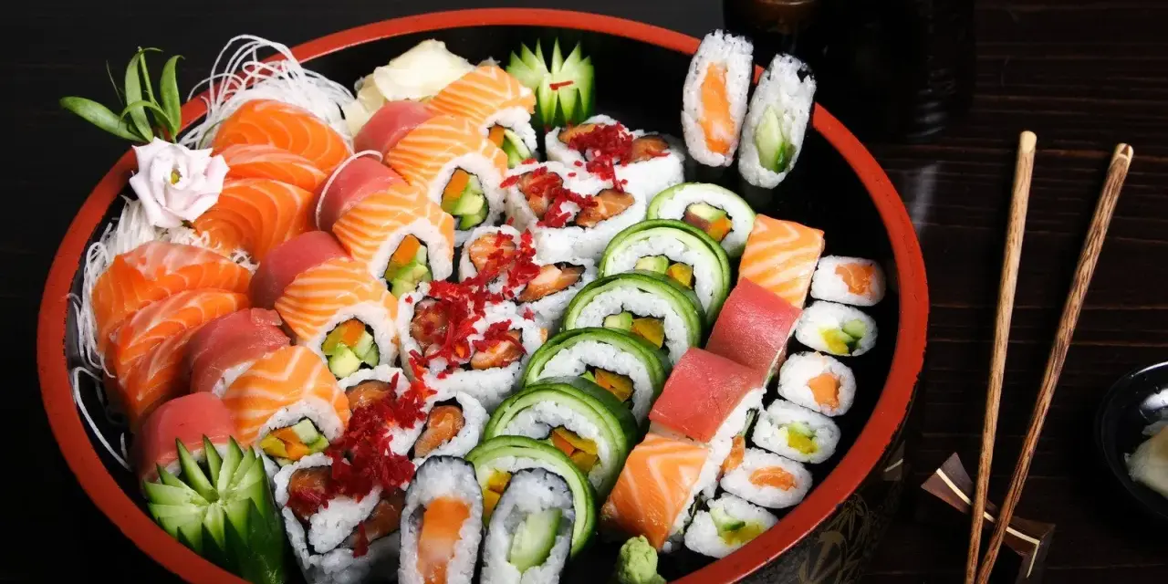 Talerz pełen różnorodnych sushi, w tym nigiri z łososiem i tuńczykiem, rolki z ogórkiem i awokado, a także kilka kawałków temaki sushi.