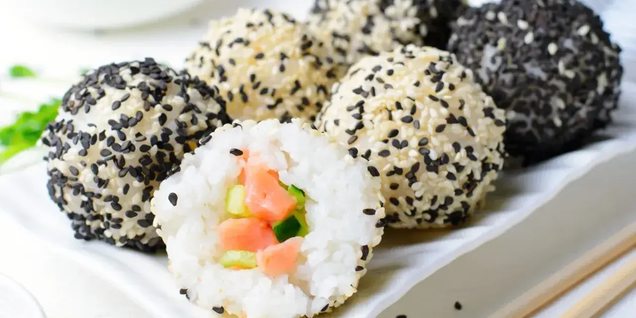 Kuliste sushi, obtoczone białym i czarnym sezamem, z widocznym wnętrzem z łososiem i ogórkiem. Prawdziwa uczta dla miłośników kuchni japońskiej.
