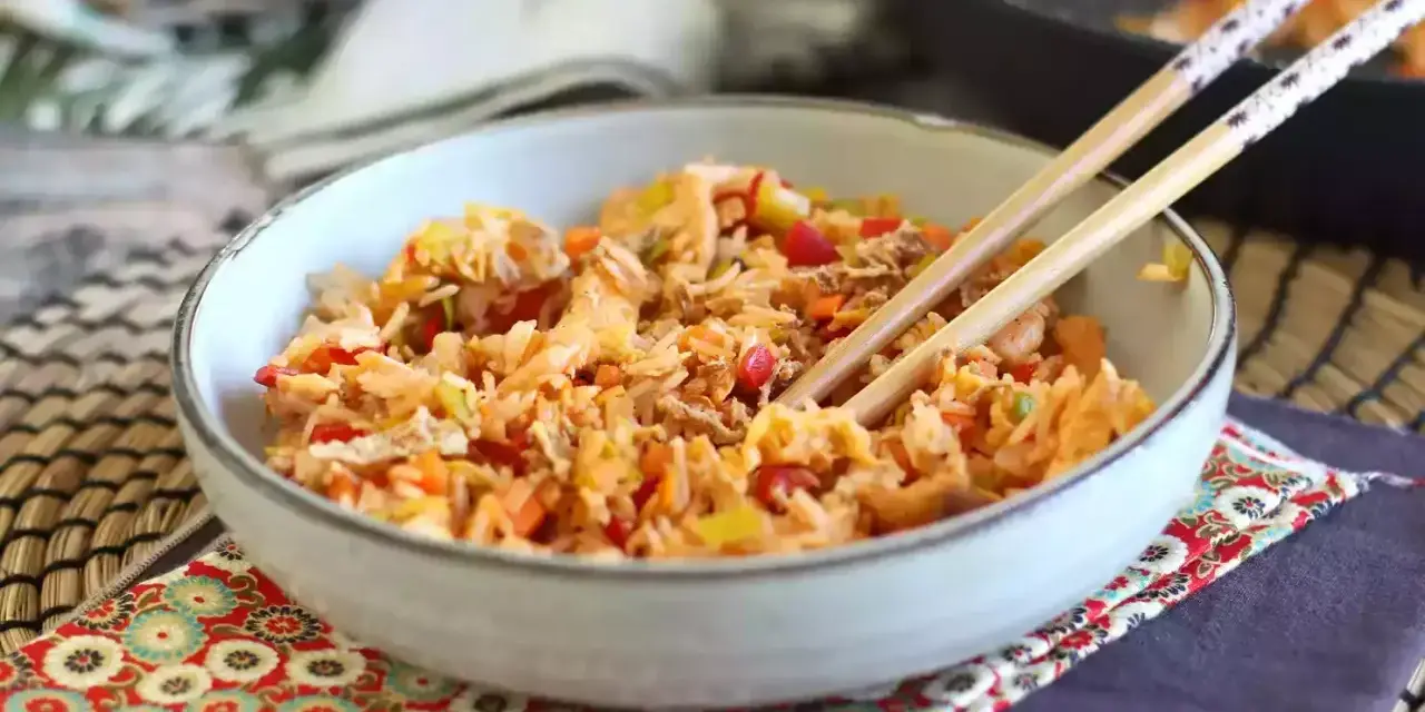 Miseczka pełna aromatycznego nasi goreng z warzywami i kawałkami mięsa, gotowa do jedzenia pałeczkami.