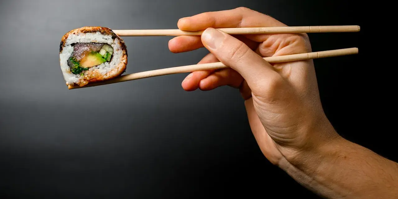 Dłoń trzyma pałeczkami jedno sushi. Zastanawiasz się, ile sushi na osobę będzie idealne na kolację?